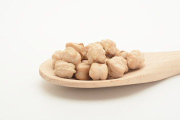 Garbanzos gordos crudos en una cuchara de madera sobre fondo blanco.