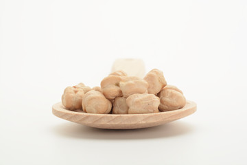 Garbanzos gordos crudos en una cuchara de madera sobre fondo blanco.