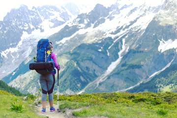 Woman hiking in mountain range. Rear view of a female backpacker walking on a small foot path in a mountain landscape. Image for trekking, hiking or climbing.