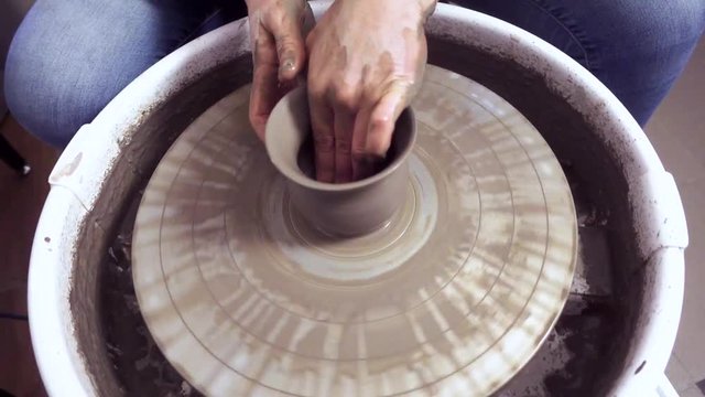 Woman making a clay pot on potter's wheel.