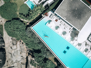 Top view aerial photo of a seductive sexy model in beige swimwear is enjoying relax in luxur villa pool during her summer weekend. Amazing fashion woman in bikini having luxury spa rest. Phuket. 