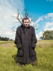 A young man wearing a long dark jacket in front of a sinister dead tree in the middle of a...