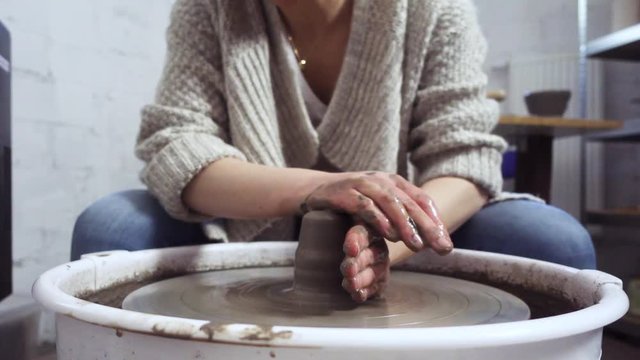 Woman shaping a clay pot on potter's wheel. Creative job