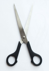 A pair of sharp metal cutting scissors with the cutting blades open. scissors for craft isolated against a white background. Black handle.