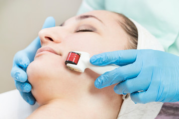 The woman undergoes the procedure of medical micro needle therapy with a modern medical instrument derma roller.