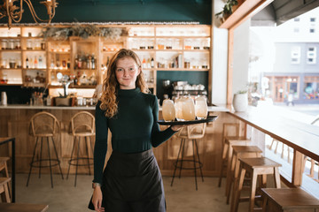 Smiling young waitress standing with a tray of drinks