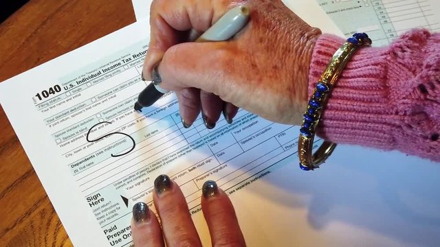 Woman's hands writing Scam on a federal tax form with a marker in slow motion. The hands are Caucasian. She has long nails nail polish.