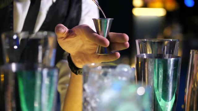Close up of barman skillful hands filling steel jigger with liquor from bottle measuring alcohol needed for cocktail drink preparation. Professional bartender deft hands at work behind bar counter