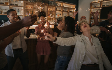 Young friends laughing and celebrating with sparklers in a bar