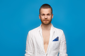 Elegant man with a beard in a white linen mint jacket on a naked body on a blue background.