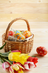 Easter eggs in wicker basket and colorful tulip flowers on wooden table background with space for text