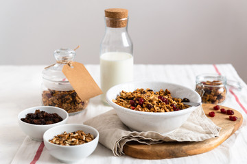 Morning granola breakfast with raisins, cranberries and hazelnuts served with almond milk on a white linen table cloth. Side view