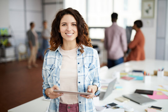Waist up portrait of contemporary woman posing at workplace and smiling at camera, copy space