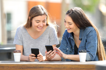 Two friends comparing their smart phones in a park