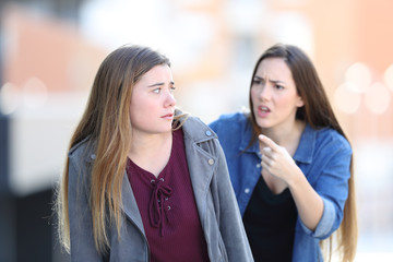 Angry girl scolding her confused friend in the street