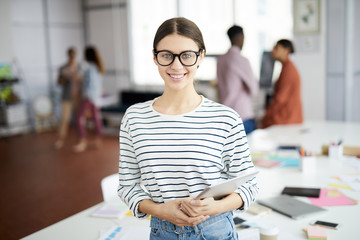Waist up portrait of creative young woman smiling at camera while posing in modern office, copy...