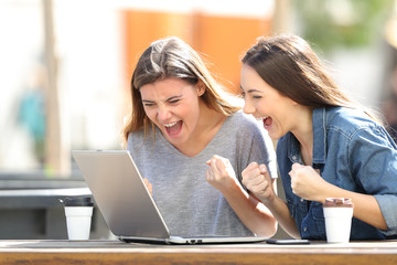 Excited women checking laptop content in a park