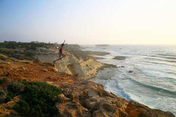 man jumping off a cliff at sea at sunset