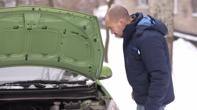 broken car. the man does not know what to do picking under the hood. winter