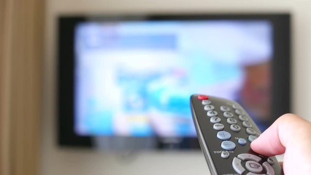 Entertainment- The man with the remote control in hand watching the  TV channel and presses the button on the remote control. Remote control in hand closeup.