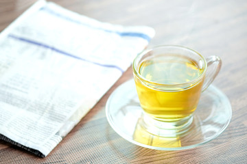 Cup of green tea hot on the desk has a newspaper and a tablet. at office