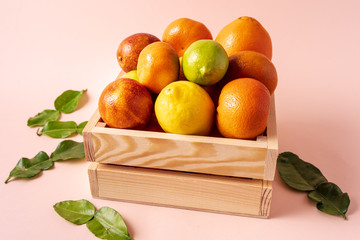 citrus fruits in a wooden crate against a pink background