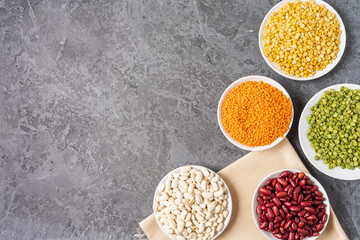 Top view of assortment of peas, lentils, beans and legumes over gray background.
