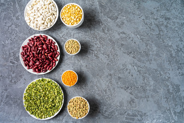 Top view of assortment of peas, lentils, beans and legumes over gray background.