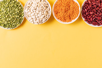 Top view of assortment of peas, lentils, beans and legumes over yellow background.