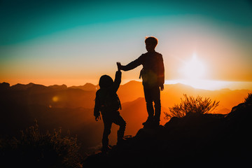 Fototapeta na wymiar Silhouettes of happy little boy and girl hiking at sunset mountains