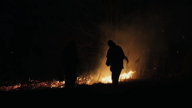 Two firefighters with fire flappers extinguish a fire at night