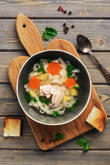 Chicken noodle soup on a cutting board with toast, wooden plank table. Top view, flat lay.