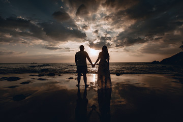 Rear view of a romantic young couple in light clothes looking at the sea. Trip to warm destination. Sunset. Phuket. Thailand