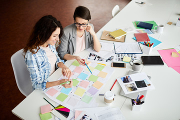 High angle portrait of two contemporary women planning project placing colorful stickers on...