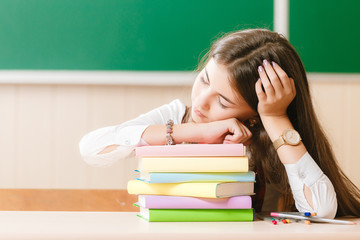 The student in school uniform sleeps on the books during the lesson. girl sitting at her desk in the classroom.