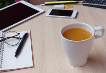 Open blank page notebook on wood table with smart phone, glasses, calculator beside in morning time business concept.