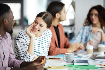 Portrait of smiling young woman talking to African-American colleague during meeting in office, copy space