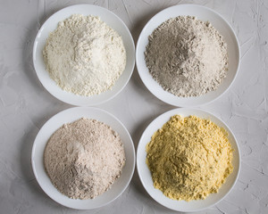 Flour from corn, wheat, rye in a plate on a gray background. copy space. The view from the top.