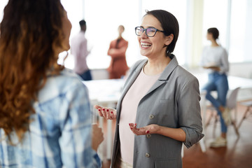 Waist up portrait of successful businesswoman smiling happily while talking to colleague in modern...