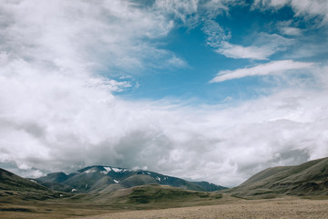 Desert green steppe of Mongolia, mountains covered with snow, blue sky and white clouds