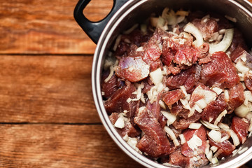 Marinated meat pieces with onions in pan on wooden background. Preparation of raw meat for barbecue. The view from the top. Raw beef mixed with onions and spices