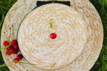 few ripe fruits of sweet cherry with twig on straw hat lying on the grass outdoors. Picnic on nature in the park close up healthy food, diet, personal care. sunny day. © Yuliia