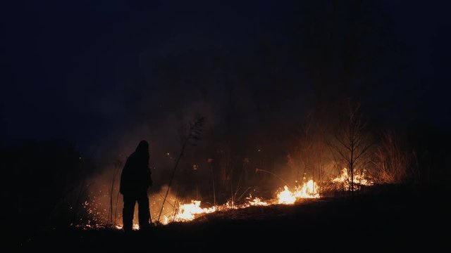 Two firefighters with fire flappers extinguish a fire in the forest