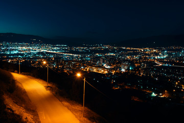Fototapeta na wymiar Night view from over capital of Georgia, Tbilisi. Street lights and hills surrounding the city. Blue sky. - Image