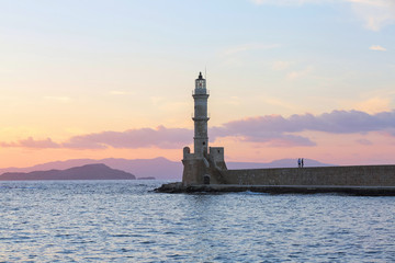 Scenery with beautiful ancient lighthouse surrounded by the sea. Sunset sky with pink light. High mountains. Location is the seaport Chania, Creete island, Greece.