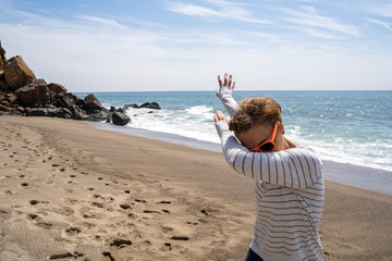 Adult caucasion woman does a dabbing dance move while on the beach. Taken at Point Dume Malibu California