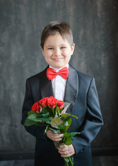 A young guy in a black suit with a red bow tie holding a bouquet of roses on a black background