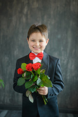 A young guy in a black suit with a red bow tie holding a bouquet of roses on a black background