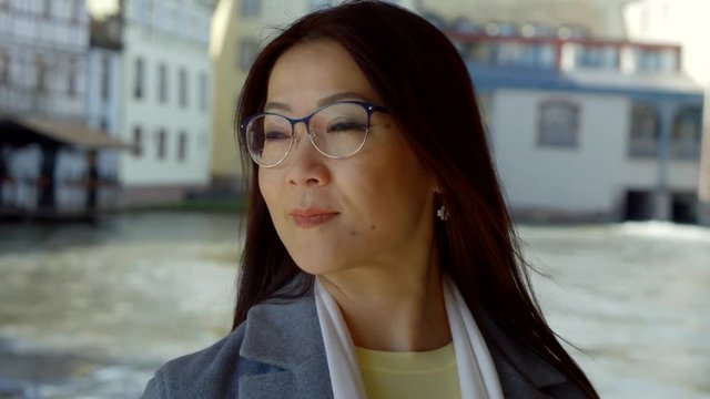 Close-up portrait of an Asian brunette girl with glasses on the background of houses and the river.