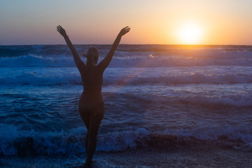 Fototapeta na wymiar Girl at sunset rejoices sea on the beach